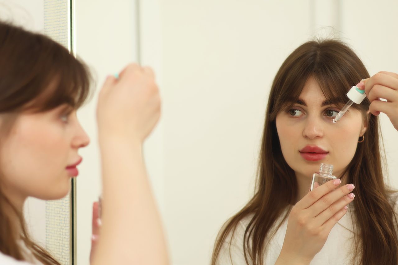 services-02 A young woman applying skincare serum in front of a mirror indoors. Perfect for beauty and self-care themes.