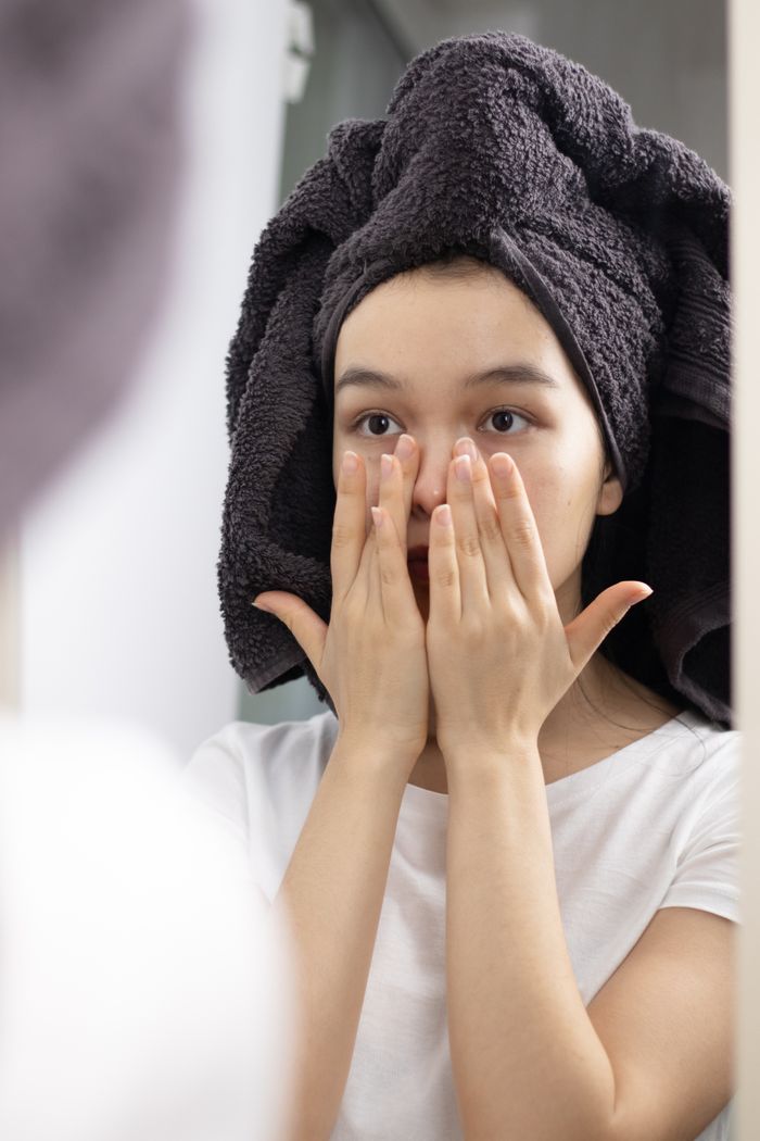 services-03 Close-up of a woman patting her face in the mirror, promoting skincare and relaxation at home.