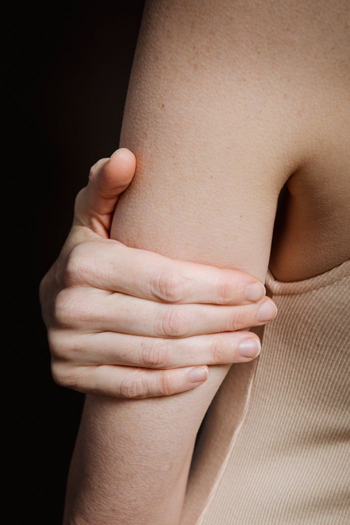 Crop anonymous person with bare shoulder and hand holding arm against black background
