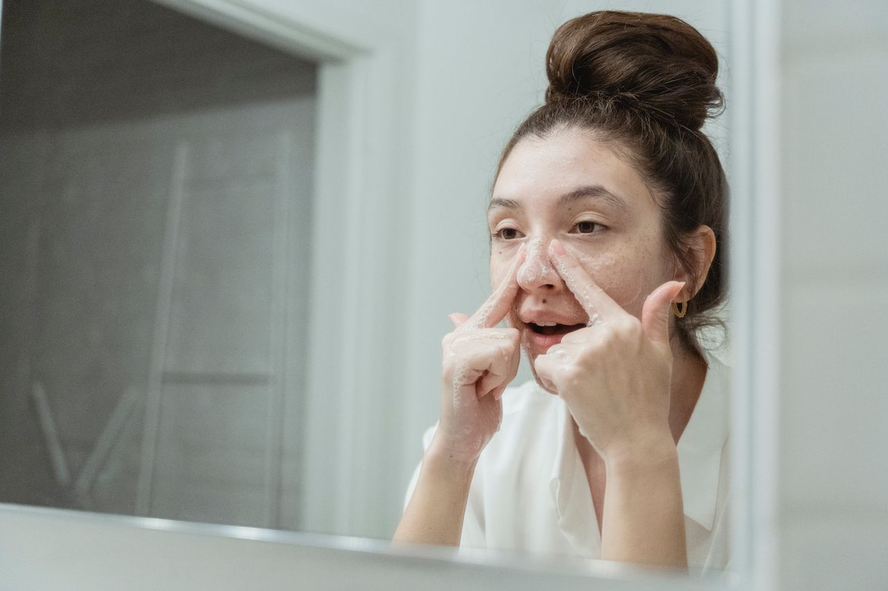 services-04 A young woman applies skincare in front of a bathroom mirror, focusing on facial care.
